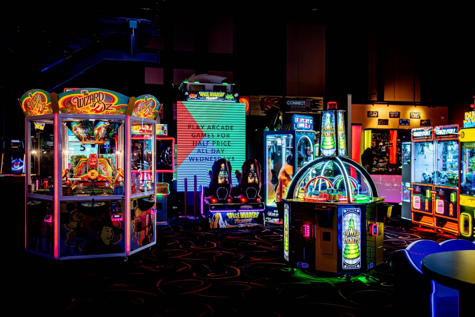 An image of the HeyDay arcade area featuring several different arcade games. The room is dark and the games are lit with neon lights.